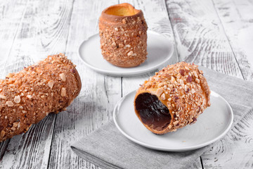Trdelnik covered in nuts and sugar with chocolate inside against white wooden background. Czech street food