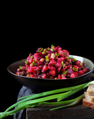 Vinaigrette salad with boiled vegetables in a clay bowl against the black background. Russian cuisine meal