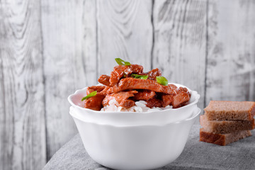 Pieces of meat in tomato sauce with spices on rice in a white bowl