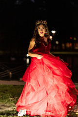 Fototapeta na wymiar Beautiful brunette in a red dress with a crown. A brunette girl dancing on night time. Artistic photo. Wedding or pregnant photosoot