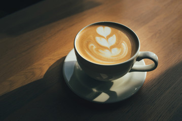 Cup of cappuccino with latte art on wooden table.