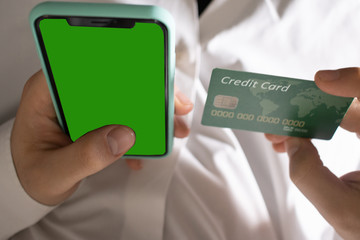 A black smartphone with green screen for chroma key compositing and a credit card in the hands of a man