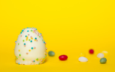 Ein Ei aus Schokalade mit bunten Streuseln aus Zucker isoliert vor gelben Hintergrund, Symbol Ostern Osterei