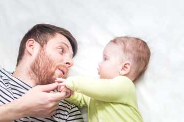 Dad and son are looking at each other while lying on the bed. Close-up portrait