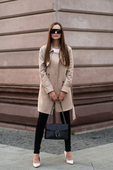 Outdoor photo of brunette lady walking on street background in autumn day.Fashion street style portrait. wearing dark casual trousers, white sweater,creamy coat. and sunglasses Fashion concept.