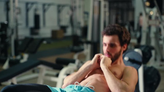 Middle shot portrait of strong bearded young man with muscular wiry naked torso doing abs exercises during sport workout training in modern gym. Concept of healthy lifestyle. Shooting in slow motion.