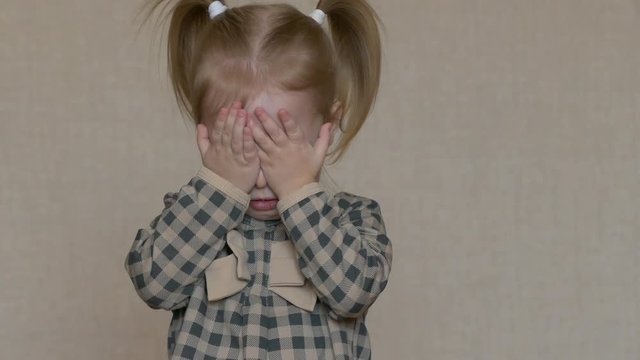 A funny little girl covers her face with her hands