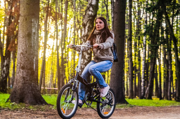Fototapeta na wymiar girl rides a black bicycle in the park among the trees in the rays of the bright sun.