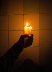 Hand holding the candle against the tiled wall