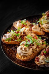 Fresh bruschettas pate in plate on black wooden table background