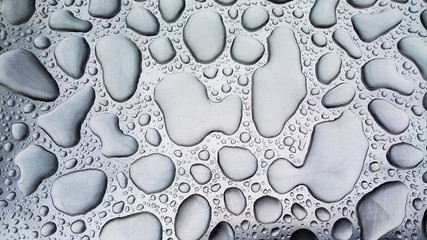 Large raindrops lying on a steel surface in a monochrome color.