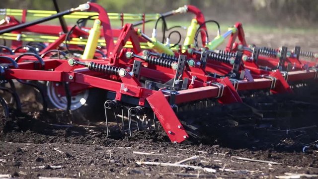 red cultivator plows the ground on the field