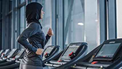 Athletic Muslim Sports Woman Wearing Hijab and Sportswear Running on Treadmill. Energetic Fit...
