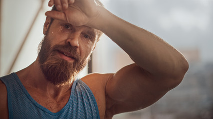 Obraz premium Portrait of Strong Bearded Male Athlete Wearing Sleeveless Shirt Wipes Sweat From His Forehead with His Muscular Hand. Handsome Man after Hardcore Exercise and Training. Man Gets Job Done