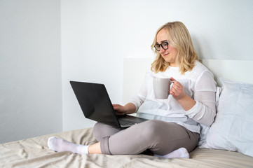 Smiling woman freelancer in glasses working at home using laptop