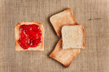Bread toe smeared with raspberry jam levitates against the background of three fried stosts lying on a burlap.