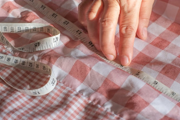 Hand of seamstress is using a tape measure to measure the size of the pink cloth close-up.