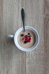 Cup of nice cream, made with frozen bananas, peanut butter and vegan milk. Frozen berries on the top. Flat lay.