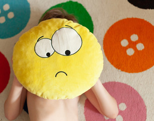 pillow sad emoji child holds hands, background carpet with colored buttons