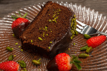 close-up slice of chocolate cake on a plate with strawberries and chopped pistachios