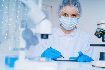 Little girl in science class with microscope on the table. Little girl scientist writing in notebook