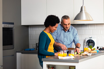 Smiling mixed race couple standing in the kitchen preparing sandwich for breakfast at home.