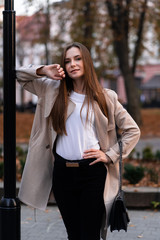 Outdoor fashion portrait of stylish young woman having fun, emotional face , laughing, Urban city street style wearing dark casual trousers, white sweater,creamy coat. and sunglasses Fashion concept.