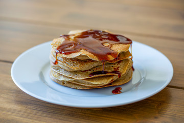 Stack of homemade plain American style pancakes with golden syrup poured over them on wooden table