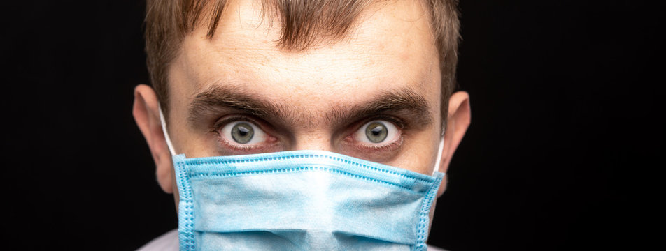 Closeup portrait of a young man in a medical mask on a black background. quarantine. restriction on movement. protection against infections and bacteria. panoramic photo.