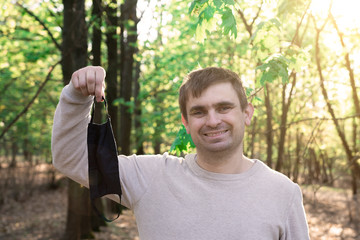 young man in the park with a smile holds a medical mask in his hands. quarantine end. infection...