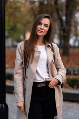 Fototapeta premium Outdoor fashion portrait of stylish young woman having fun, emotional face , laughing, Urban city street style wearing dark casual trousers, white sweater,creamy coat. and sunglasses Fashion concept.