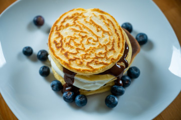 Pancakes with maple syrup and blueberries on a white plate with a wooden table as background or background. Sweet tasty breakfast or also as a delicious dessert. American pancakes with berries.