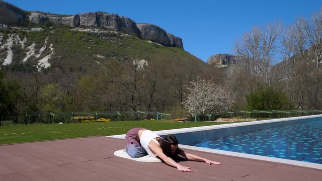 Open air stretch. Yoga. By the pool. The girl with long dark hair doing yoga.