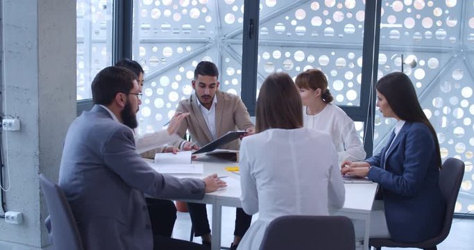 Team of mixed-races male and feamle business partners sitting together at meeting at table and having talk. Multiethnic men and women working at desk and planning future of company. Brainstorming.