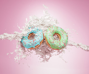 Two donuts with icing and sprinkles on a uniform pink background, and milky splash.