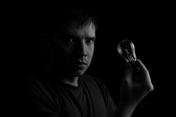 Young man and electrical bulb against dark background
