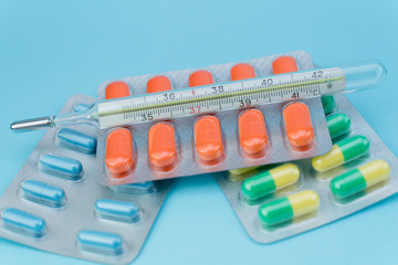 blisters with pills and thermometer lie on a blue background