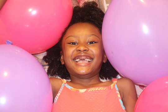 Adorable African American Child Smiling surrounded by Pink and Purple Balloons