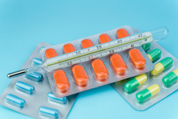 blisters with pills and thermometer lie on a blue background
