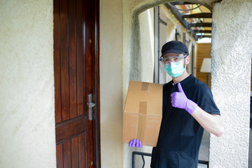 Fototapeta na wymiar portrait of handsome male delivery man delivering parcel to female client at home with mask gloves and protection glasses against covid19 coronavirus virus infection