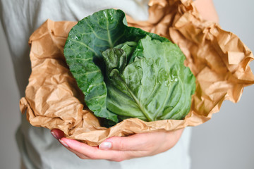 The woman holds young cabbage in her hands. Ripe fresh cabbage in paper packaging. Healthy food,...