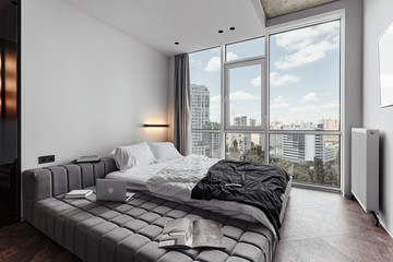 Fototapeta premium bright modern interior, bedroom in black white tones. cosy room with sofa, laptop and books in a room with panoramic windows. white sheets