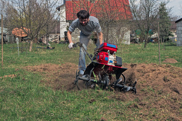 Man working in the garden with garden tiller. tractor cultivating and loosens soil field