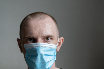 A guy in a medical mask and a black t-shirt is sitting on a light background