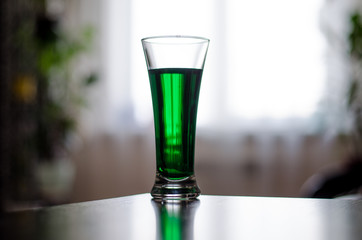 a glass of green liquid stands in front of the window