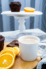Coffee with oranges in the foreground, in the background baking chocolate cupcakes.