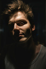 Portrait of a man in a white t-shirt, looking directly at the camera. The light falls on part of the face