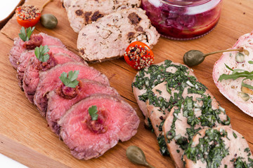 On a wooden plate, beef roast beef, herb marinated tongue, chicken terrine, duck galantin, cherry sauce