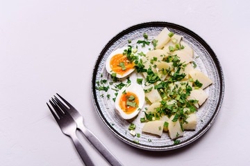 Boiled potatoes with herbs and soft-boiled eggs in a plate on grey concrete background. Selective focus