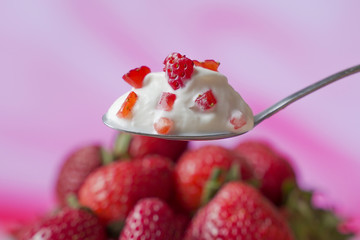 Strawberry yogurt in a spoon, against the background of fresh strawberries